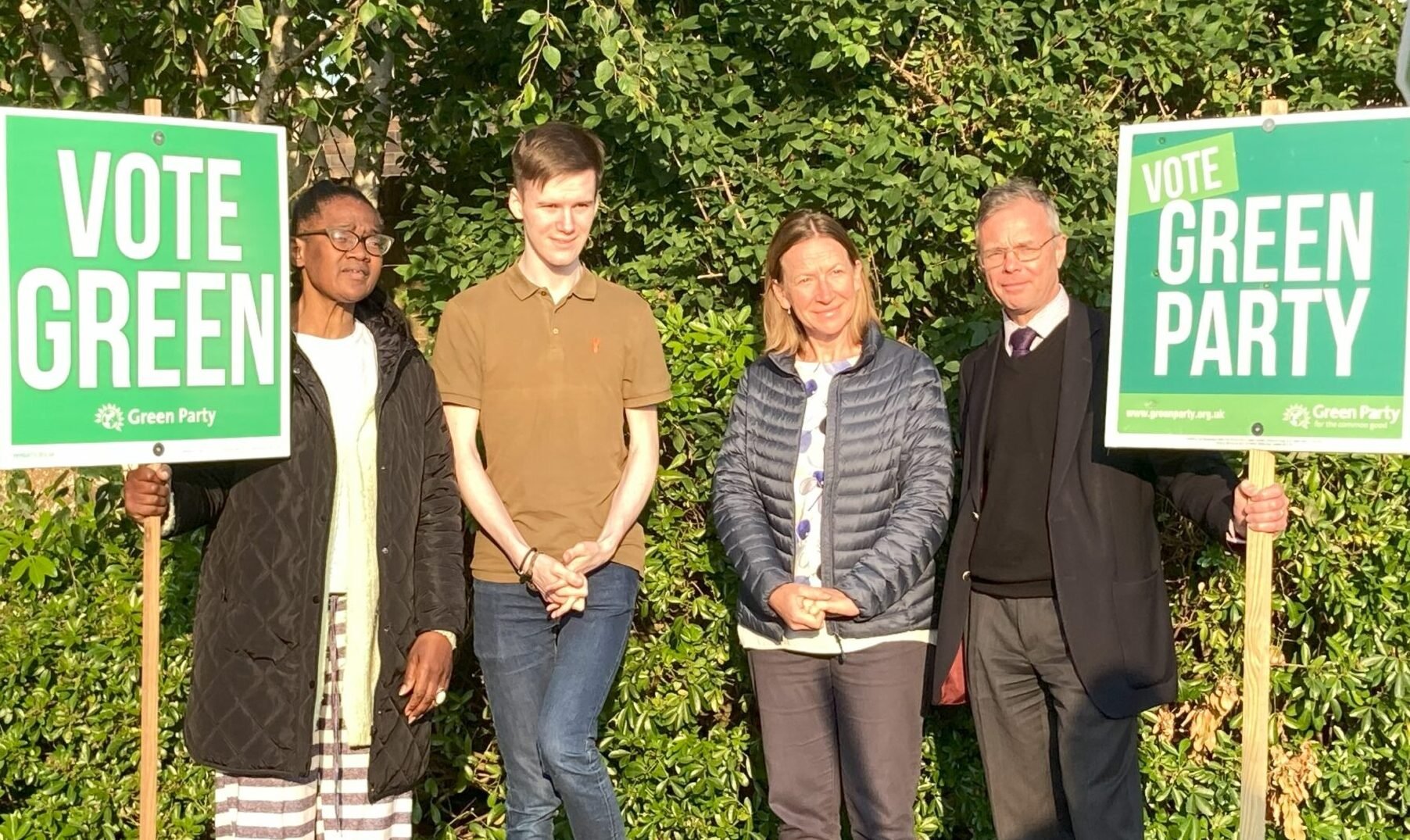 Four people in a line with large Vote Green posters.