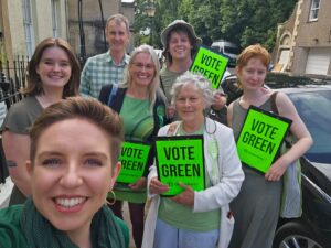 A group of people wearing green and holding Green Party posters, with Green MP Carla Denyer in the front.